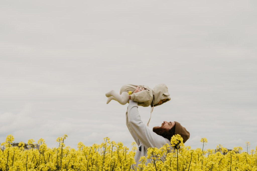 a-person-holding-a-baby-in-a-field-of-yellow-flowers-2bkv-ychru4